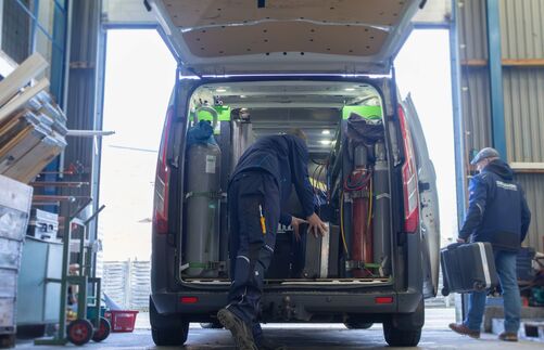 Kundenservice - Delewski Kälte-und Klimatechnik Zwei Kundendiensttechniker tragen Service-Koffer in den Firmenwagen, der in einer Halle steht.