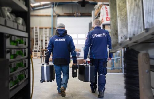 Zwei Kundendiensttechniker in einer Halle von hinten während sie gehen und einen Service-Koffer tragen.